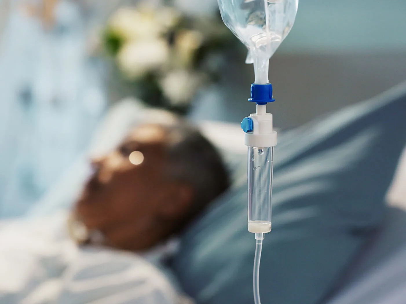 A drip line in the foreground and a bed bound hospital patient in the background