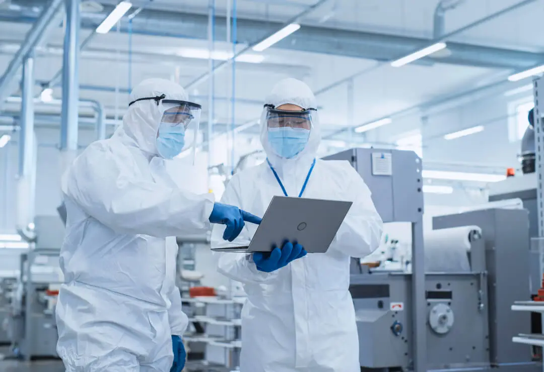 Technicians look at a laptop together with equipment in the background.