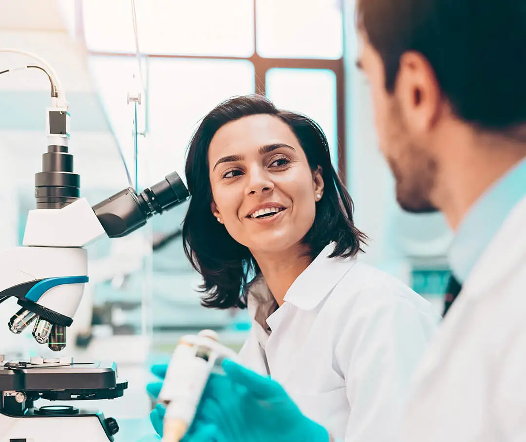 Two technicians in discussion while working in front of a microscope