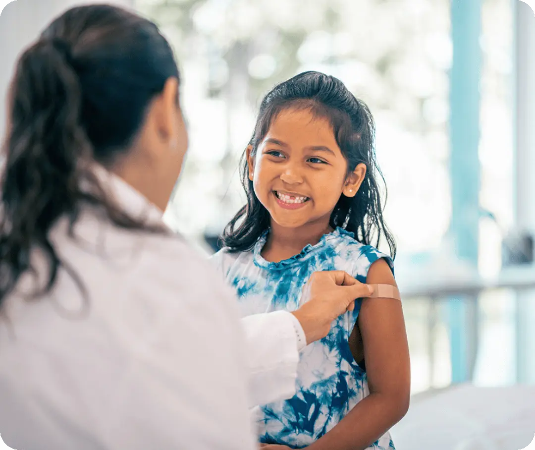 A nurse places a bandaid on the arm of a smiling child.