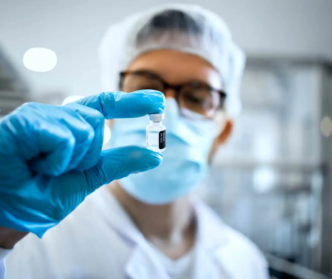 A technician holds a small bottle in front of his face.