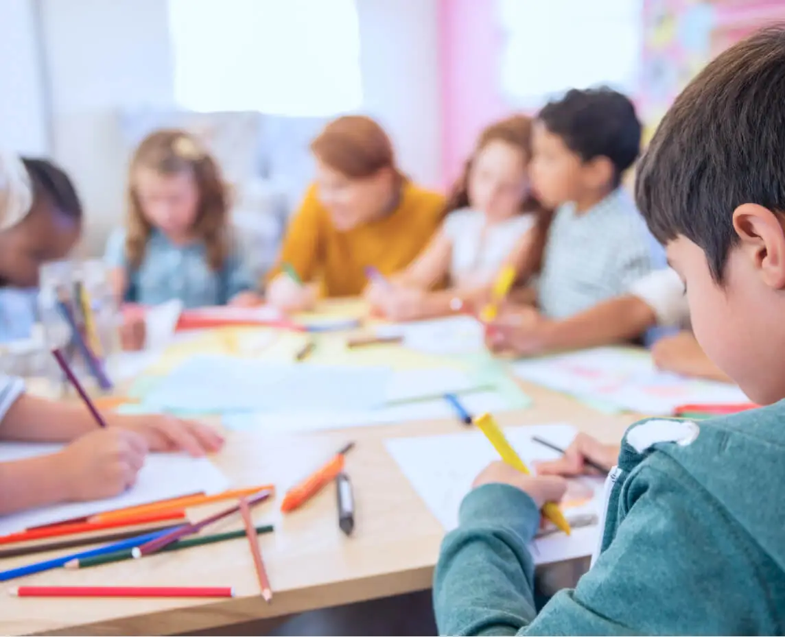 A group of children work sit at a table and work on an art project.