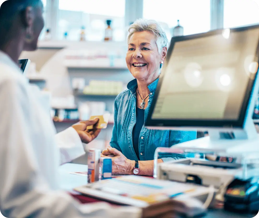 A woman smiles and pays for her prescription at a pharmacy.