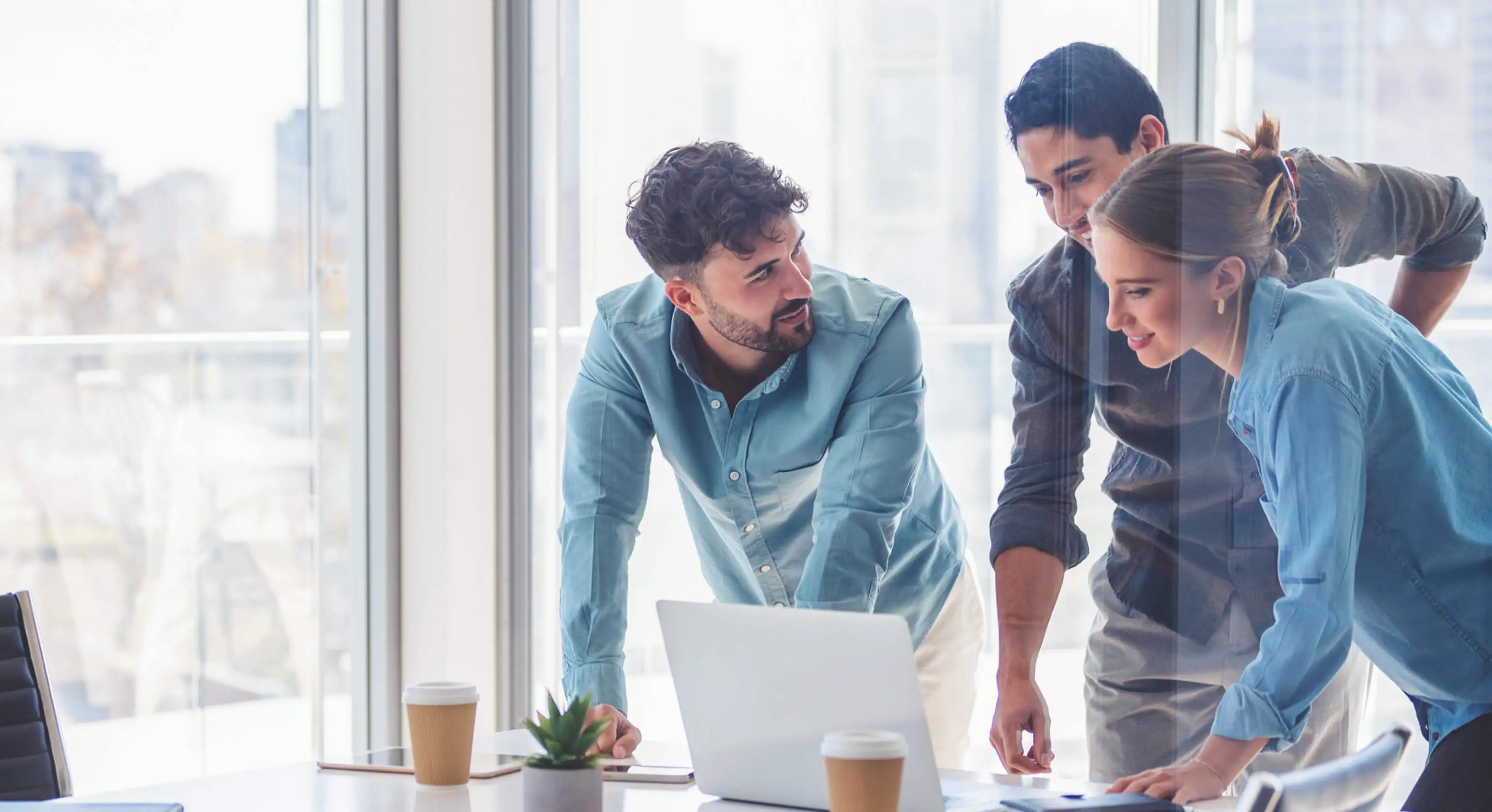 A group of colleagues discuss what they see on a laptop screen.