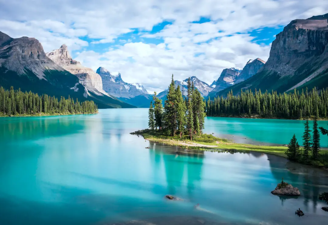 A cluster of trees on a peninsula in the middle of.a lake surrounded by mountains.