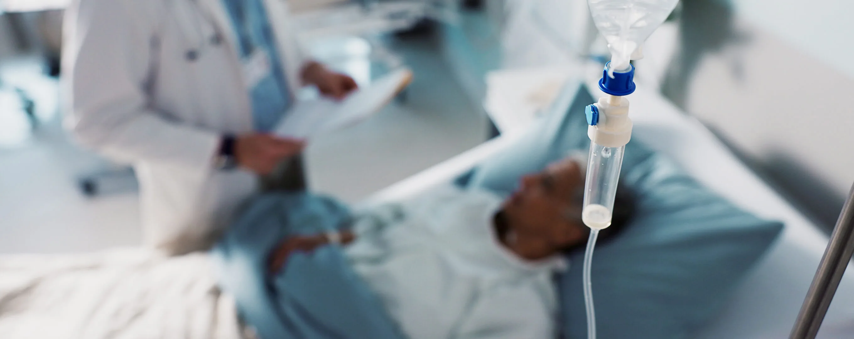 A drip line in the foreground and a bed bound hospital patient in the background