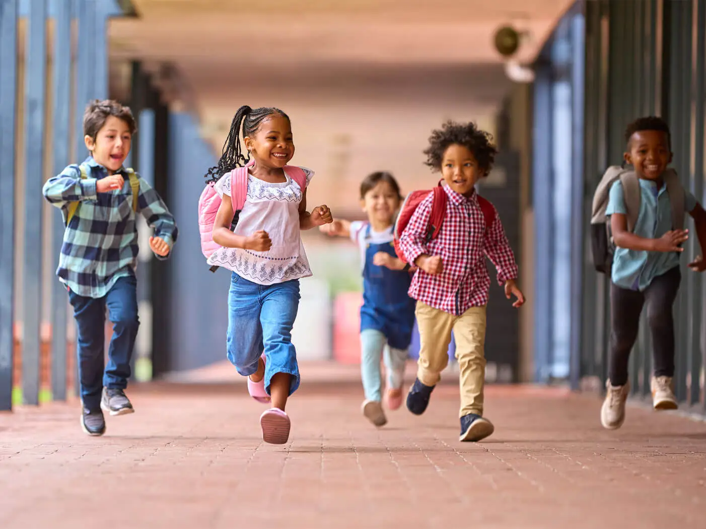 A group of young kids with backpacks running on a walkway.