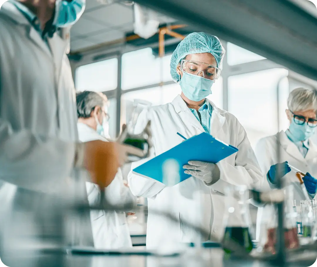 A scientist with a face mask writes on a clipboard.