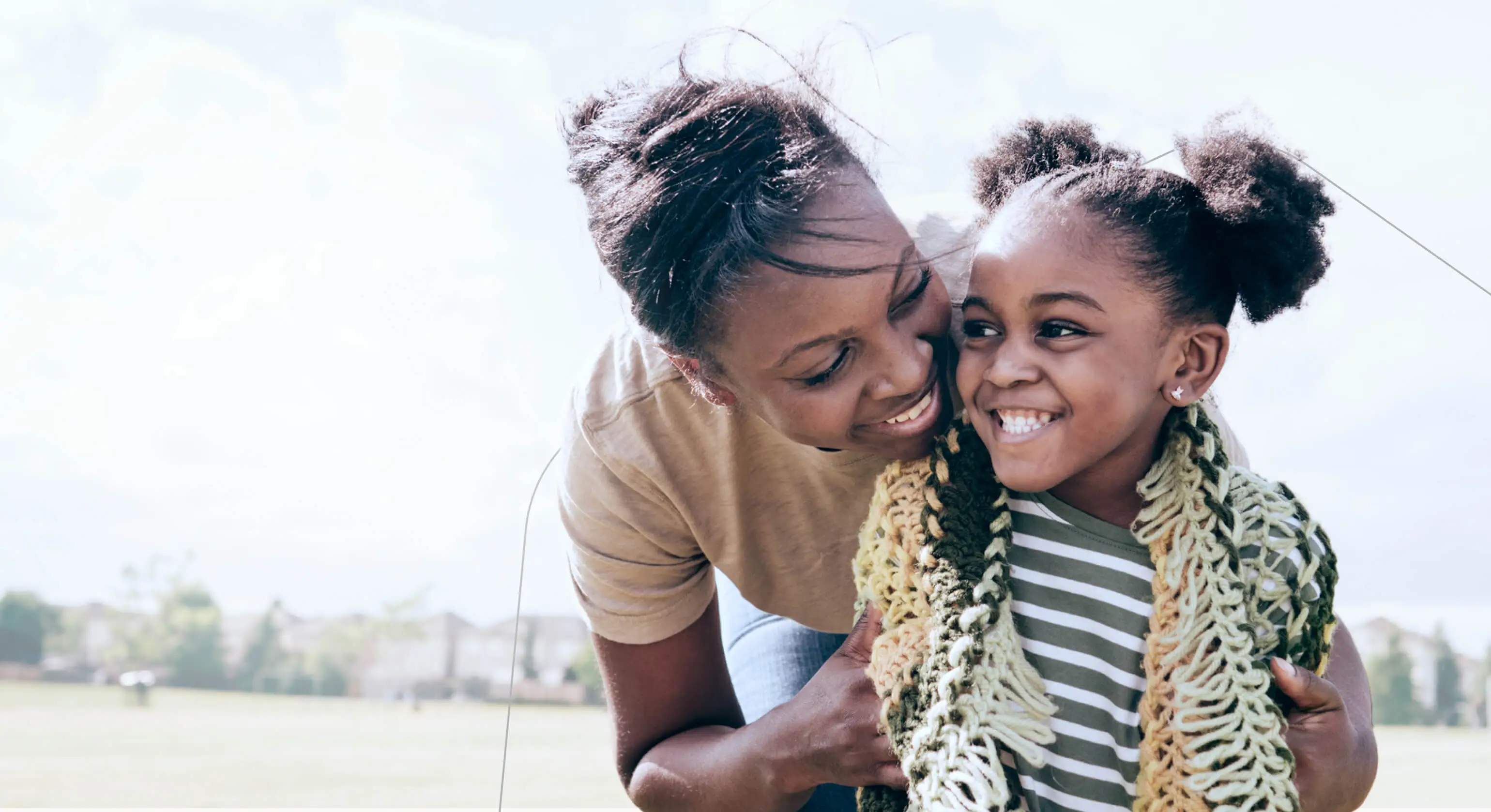 A smiling mom hugs her smiling daughter in a park.