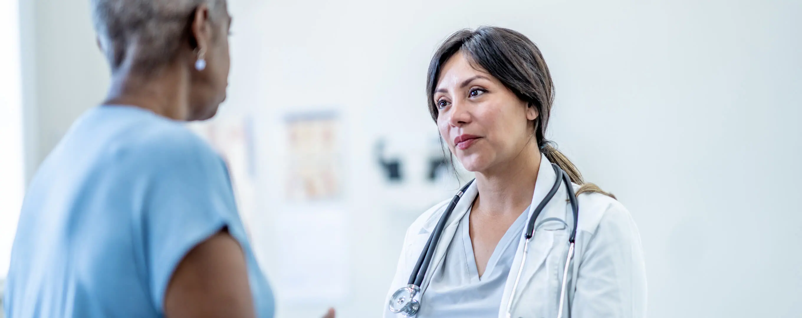 A patient sits on an examination bed and talks to her doctor.